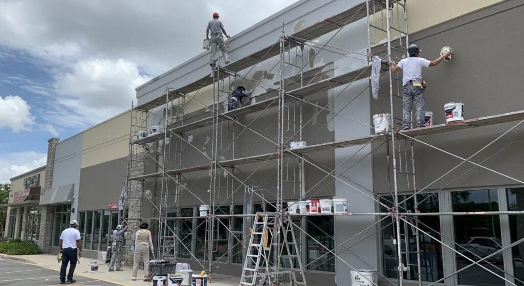 a vibrant and busy sarasota commercial district showcases a skilled contractor painting the exterior of a modern building, with scaffolding and colorful paint buckets creating a dynamic atmosphere of professionalism and local commitment.
